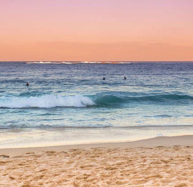 Surfers in the ocean at sunset with pink and blue sky
