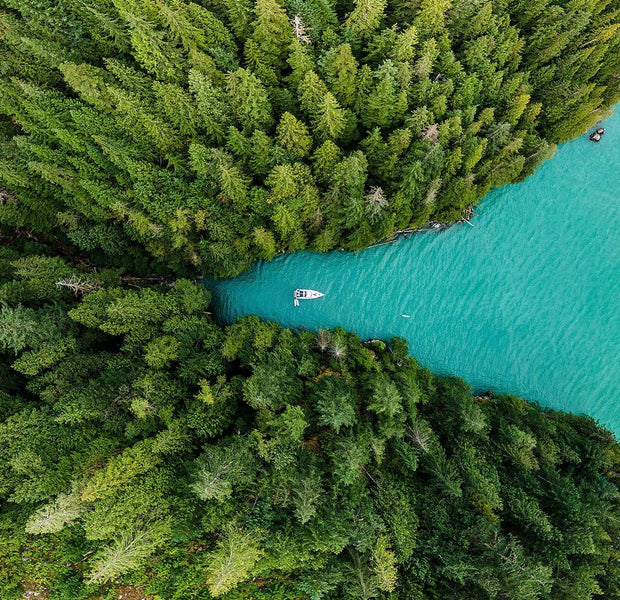 Aerial view of a boat on a turquoise lake surrounded by dense green forest.