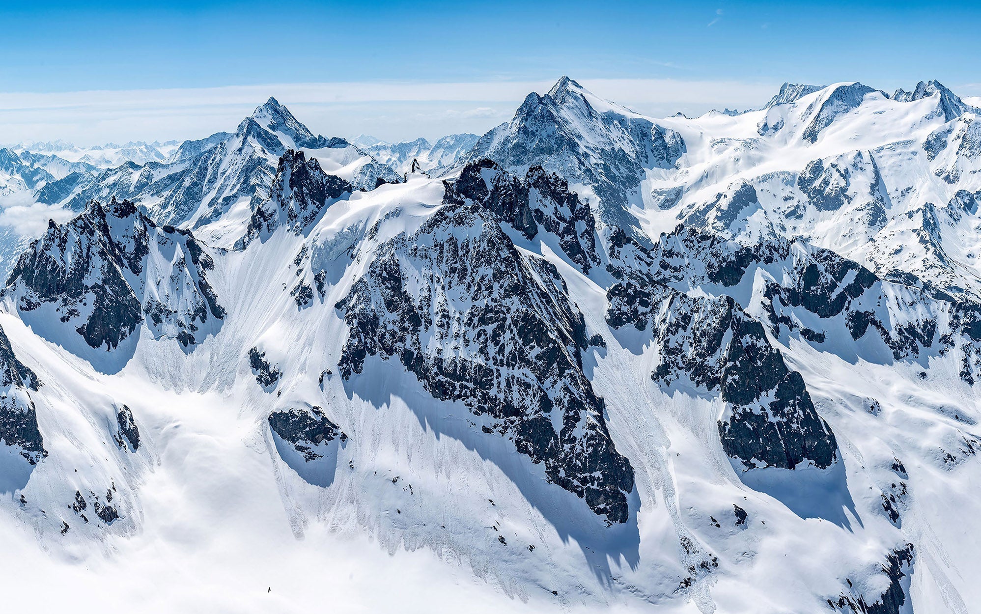 A panoramic wall mural depicting a breathtaking view of snow-covered mountain peaks under a clear blue sky.