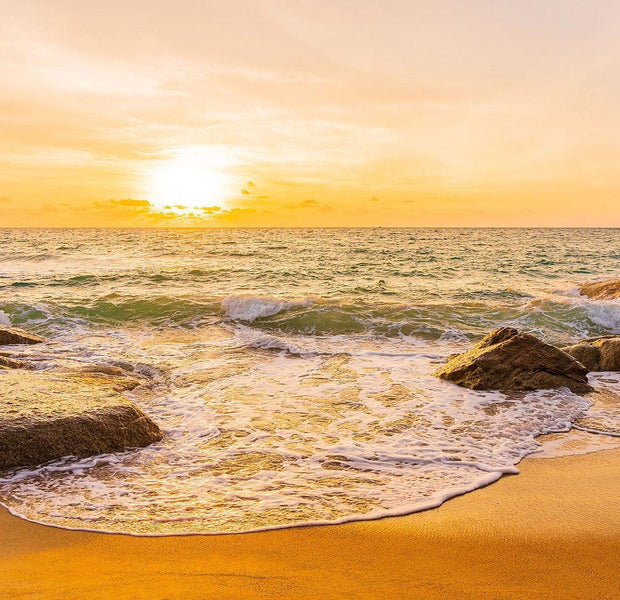 A vibrant wall mural depicting a beach scene with the sun setting over the ocean and waves crashing against rocks on the shore.