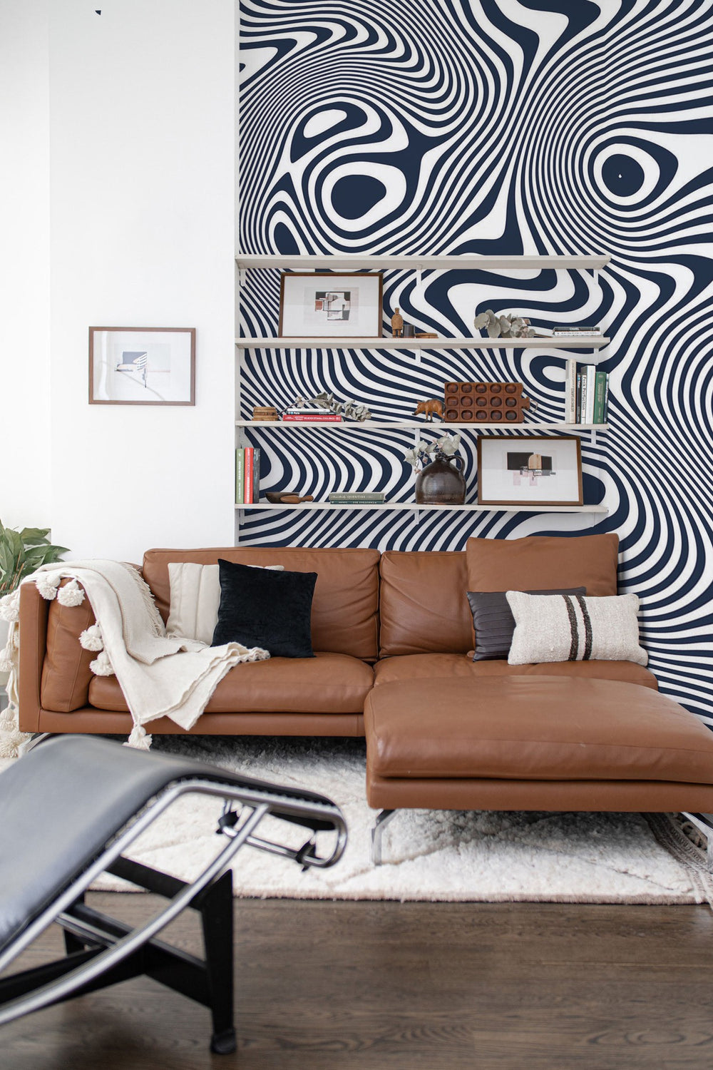 A cozy living room with a black and white abstract wall mural behind a tan leather sofa with decorative cushions and a modern black chair.