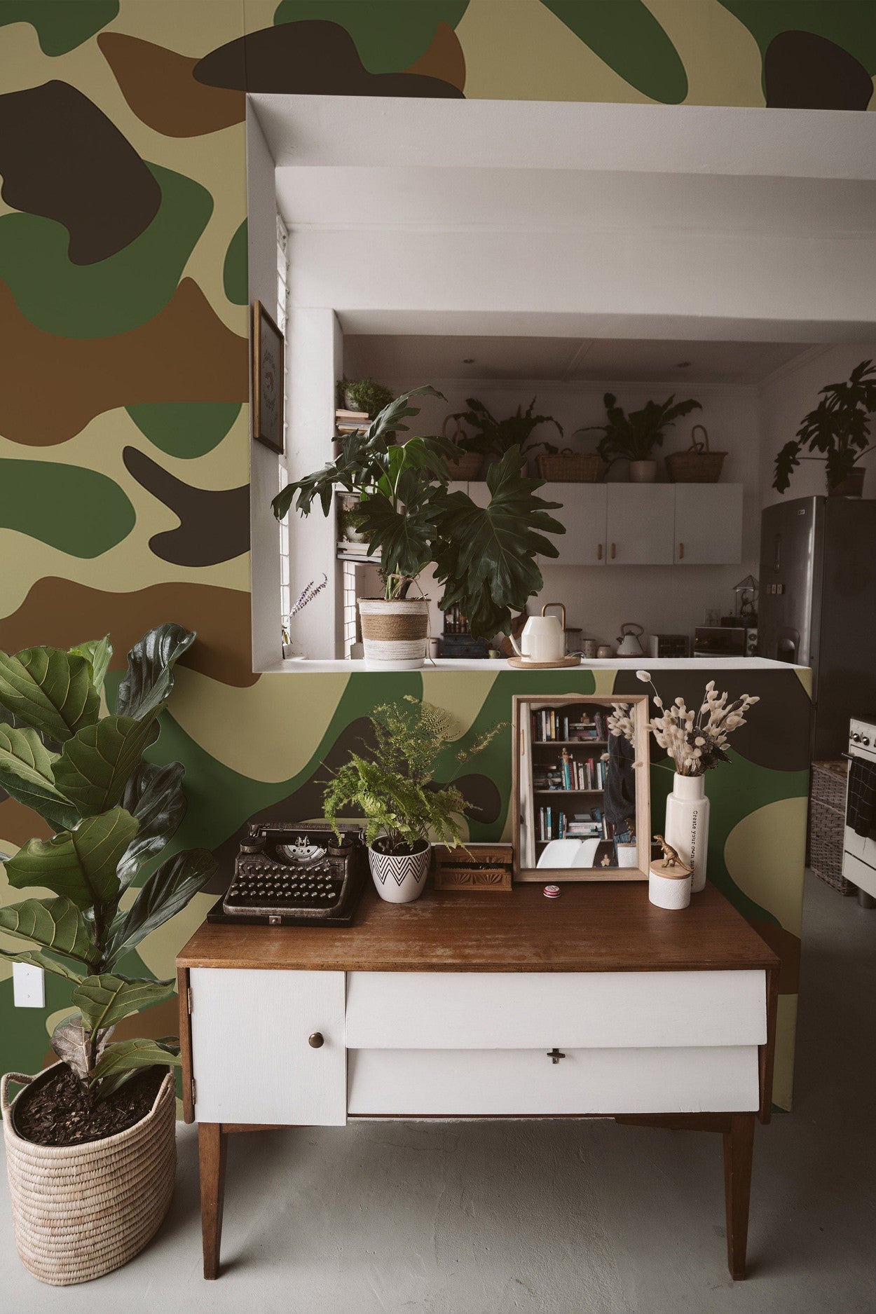 Stylish home office interior with a large camouflage pattern wall mural, vintage wooden desk, and decorative plants