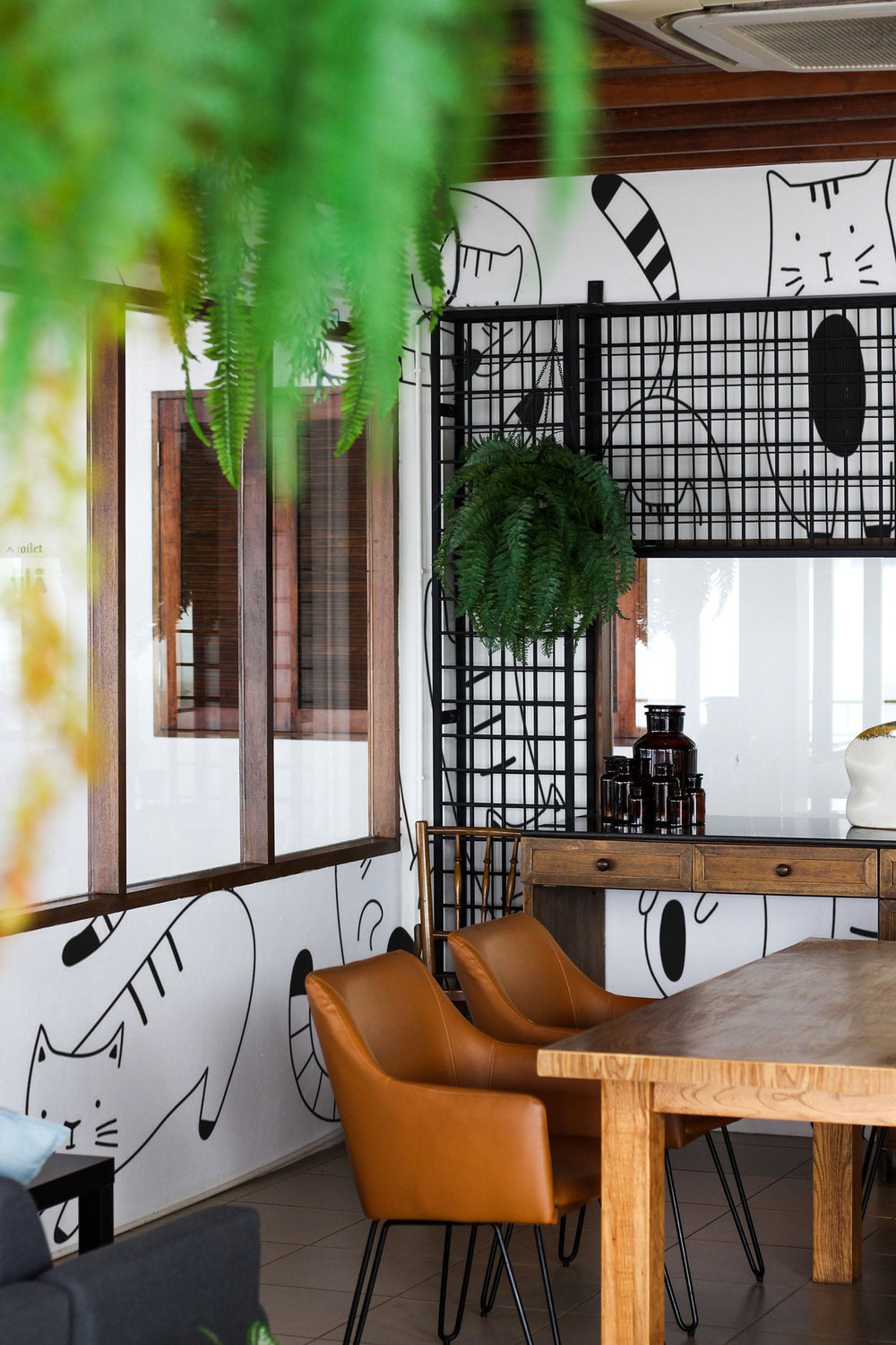 Interior view of a modern cafe with stylish furnishings and a playful cat mural on the wall.