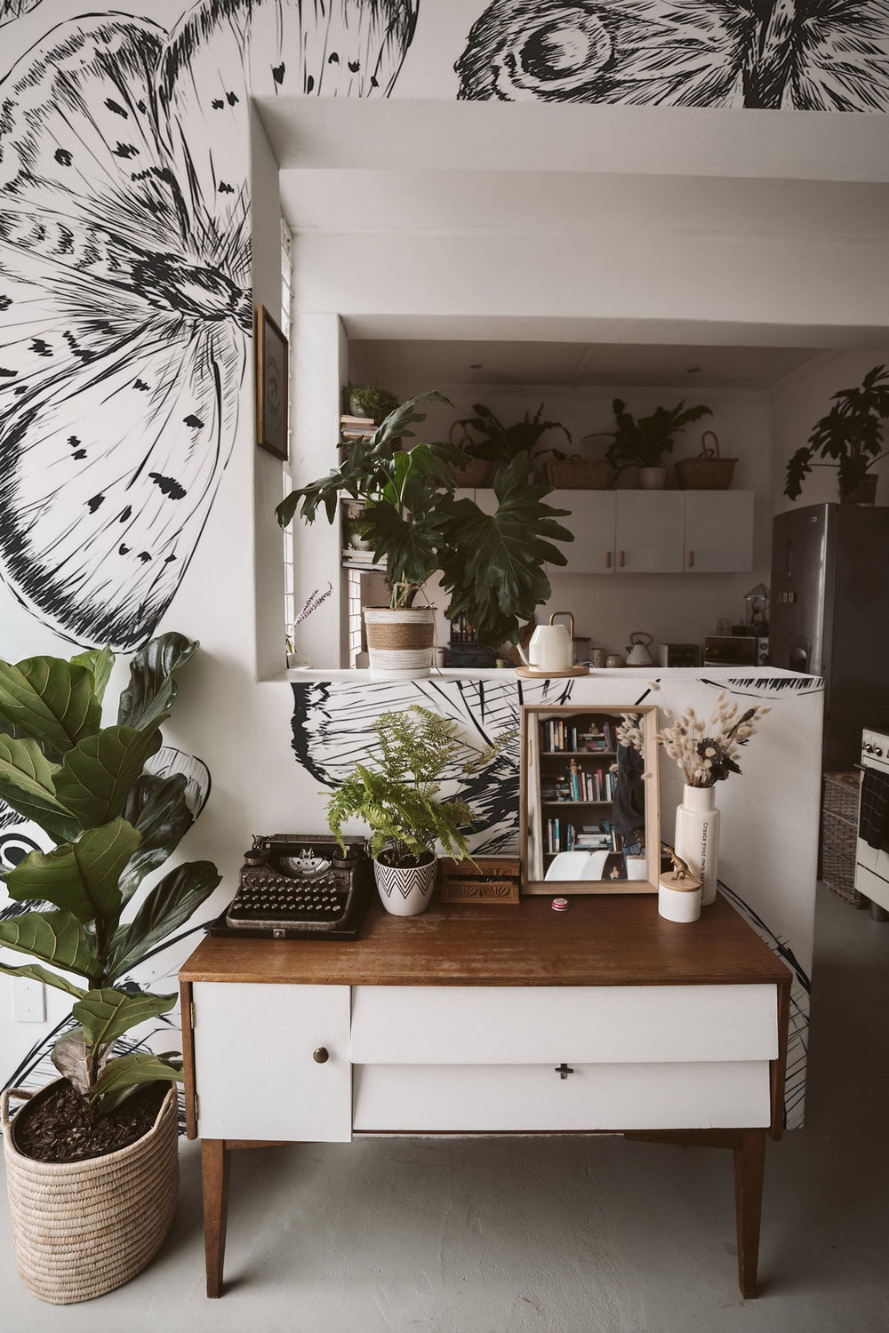 A cozy room interior featuring a stylish vintage desk, potted plants, and a striking black and white floral wall mural.