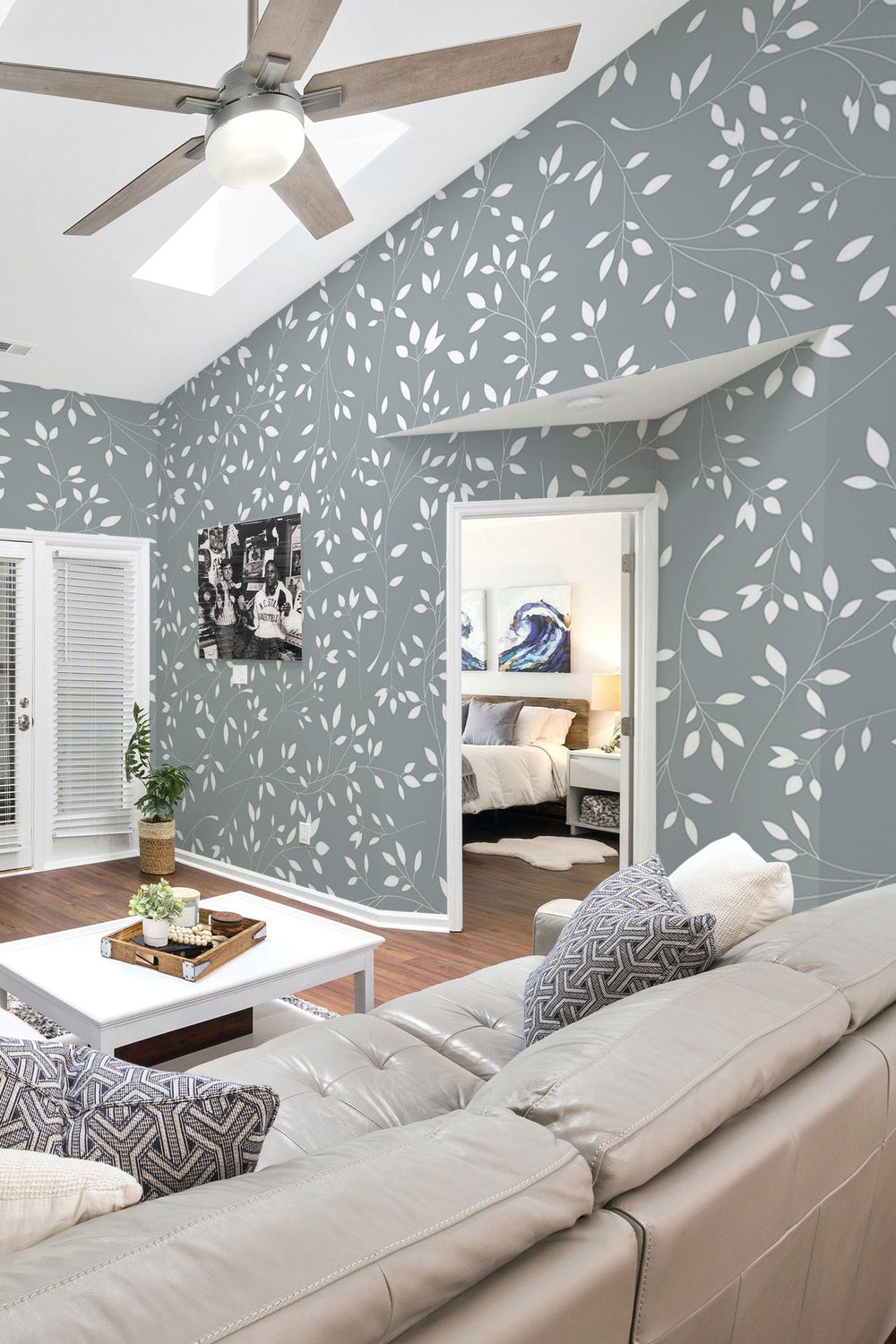 Stylish living room interior with ceiling fan and leaf pattern wall mural with a view into the adjoining bedroom