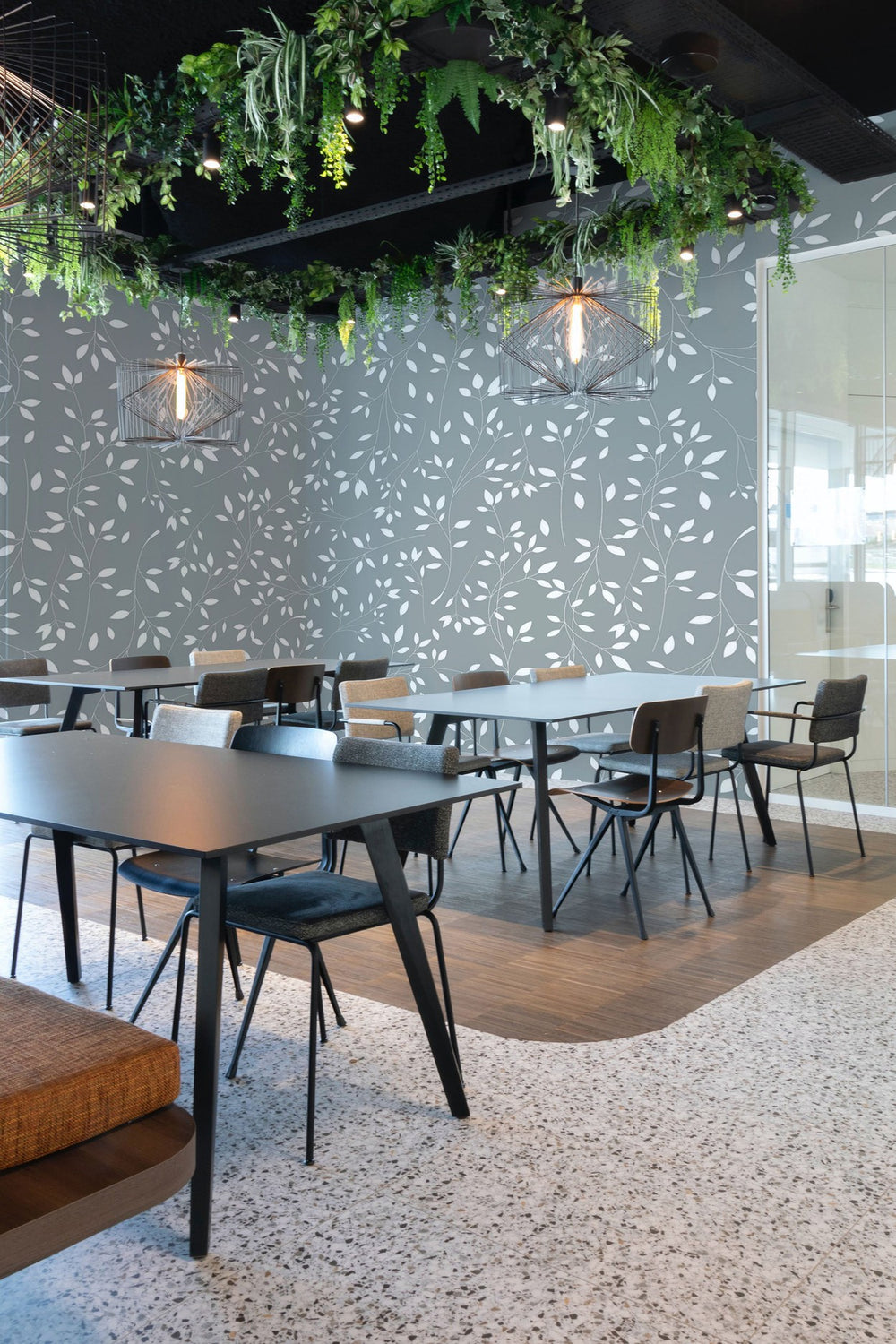 Interior of a modern office space with stylish chairs, tables and a decorative wall mural with botanical patterns