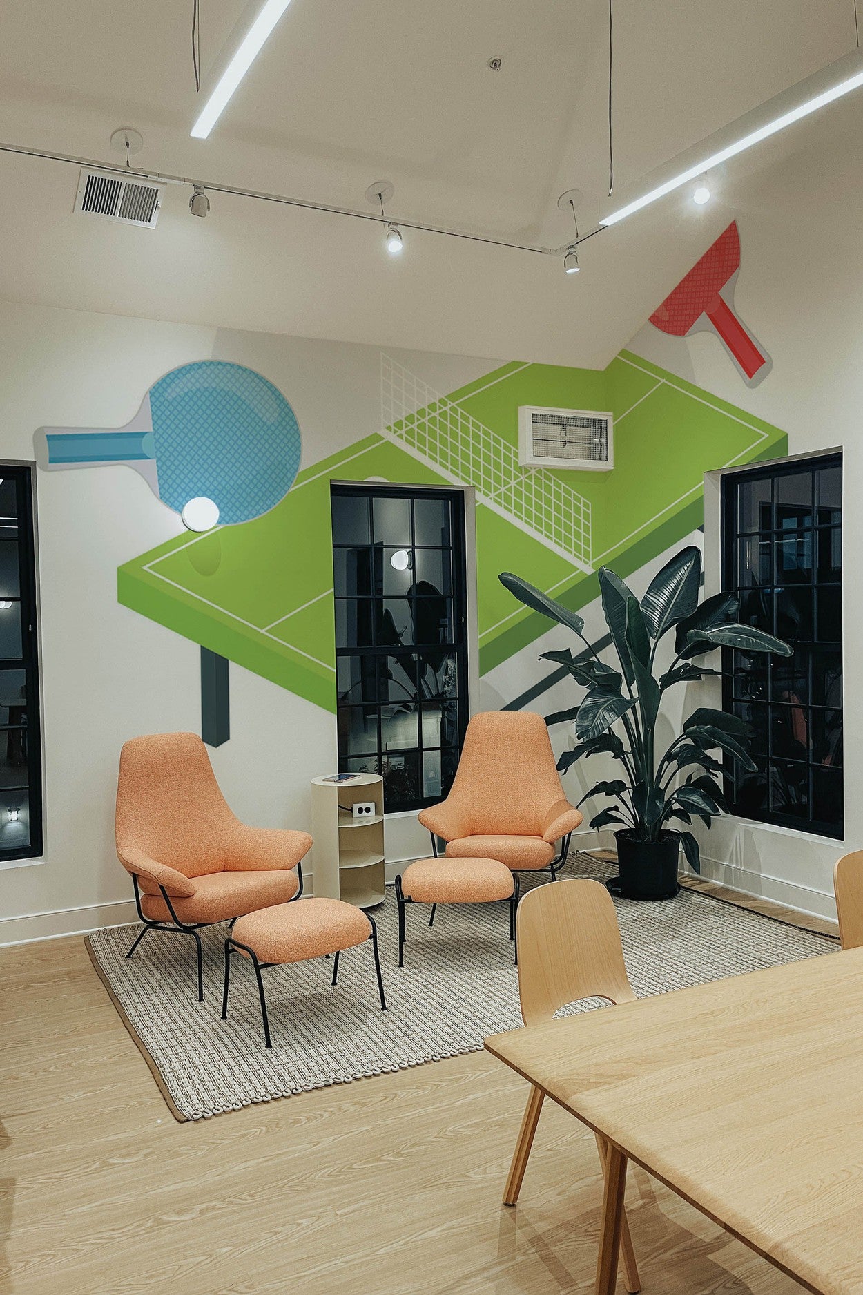 Modern office meeting room with brightly colored wall mural depicting oversized tennis rackets and a tennis ball