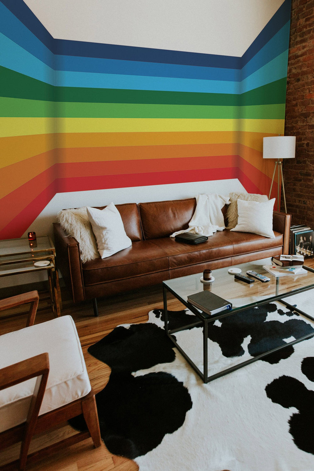 A cozy living room with a vibrant rainbow-striped wall mural, leather sofa, and modern furniture.