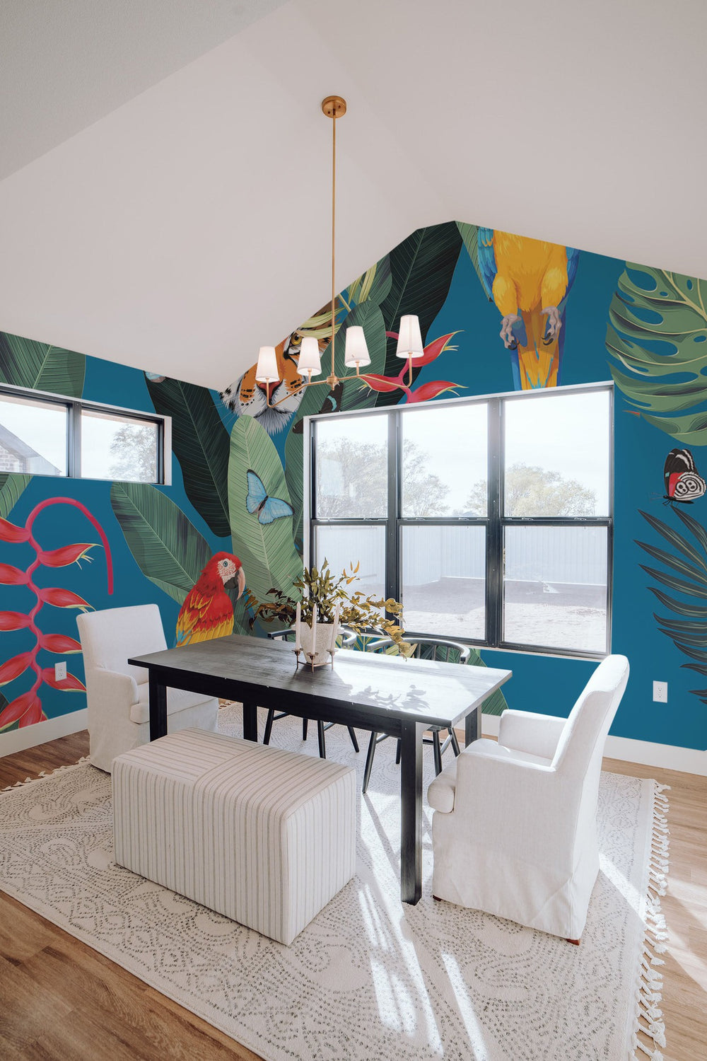 A bright interior with a tropical-themed wall mural featuring large leaves and a parrot, complemented by modern furniture and large windows.